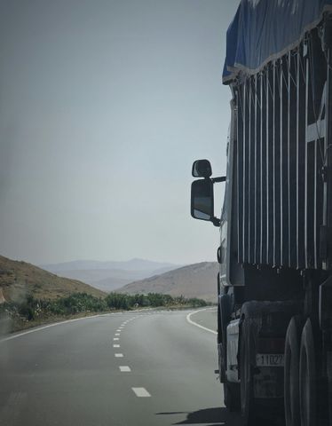 Semi-truck on a winding road through a hilly, arid landscape under a clear sky.