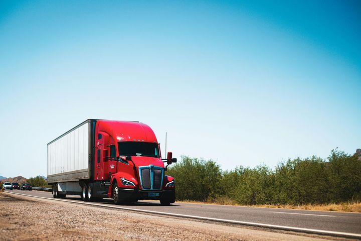 Red semi-truck driving on a highway, bright blue sky in the background.