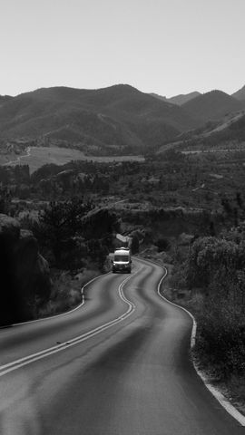 Winding road through a mountain landscape; a vehicle drives along the road toward the distant hills.