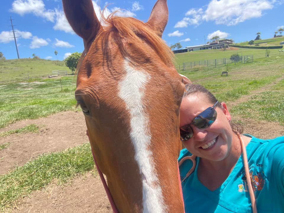 Woman smiling next to a brown horse in a sunny grassy field — Sarina Veterinary Surgery In Sarina, QLD