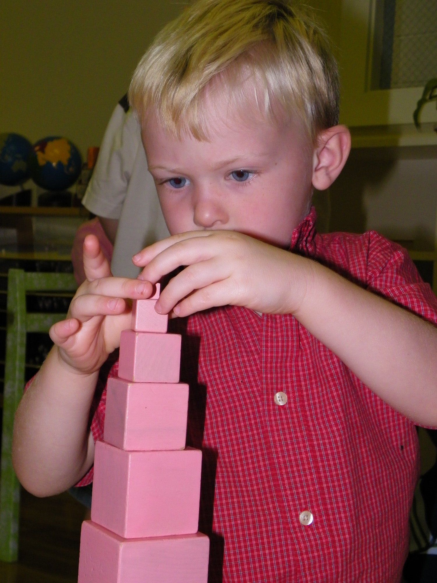 Montessori child building a tower of pink blocks, concentrating, in a classroom.