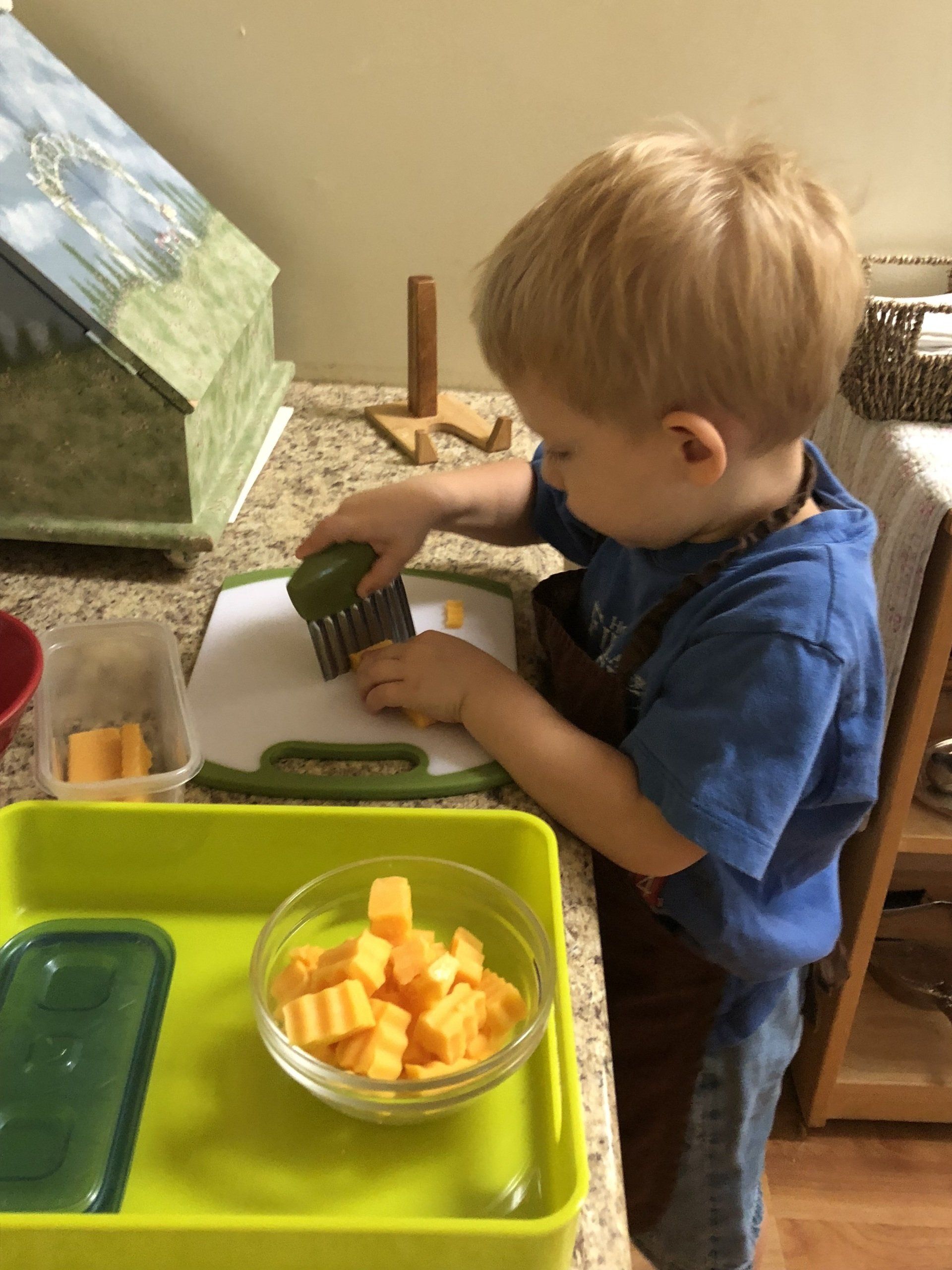 A toddler sitting in Montessori size chair cutting vegetables