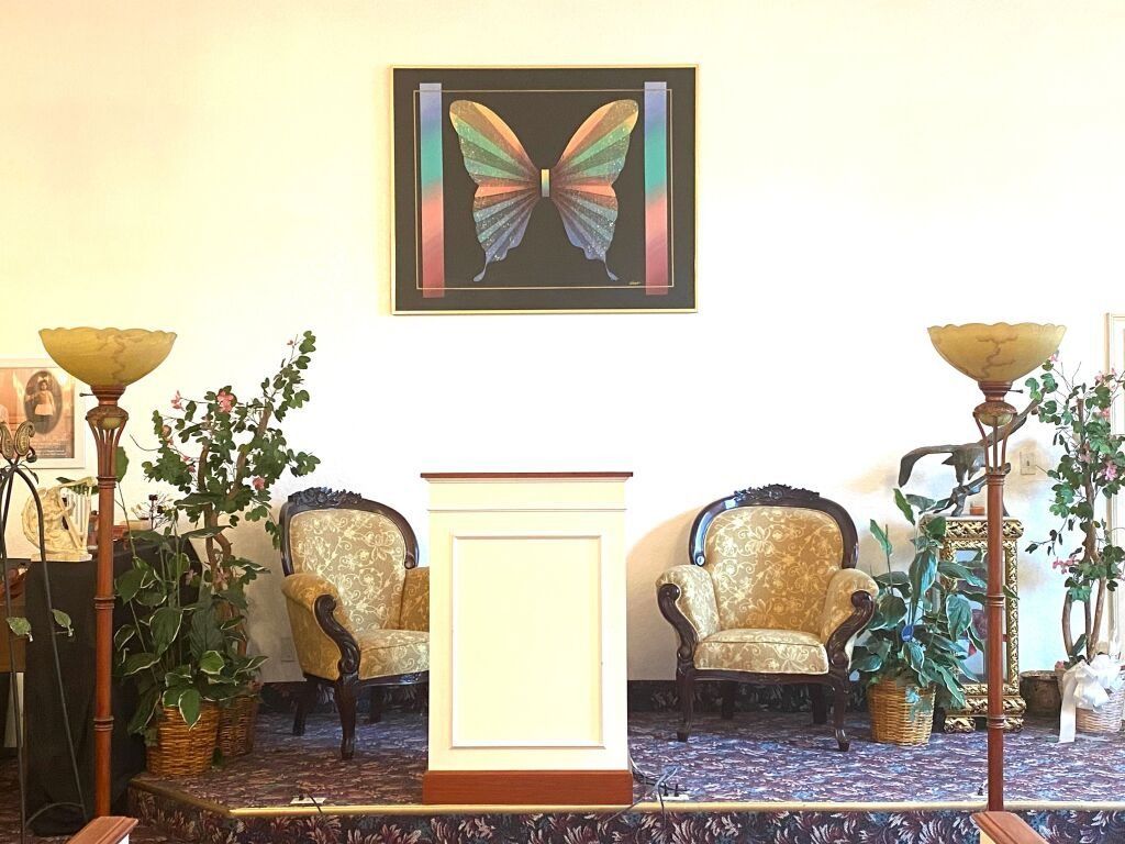 Altar area with butterfly art, podium, two ornate chairs, plants, and lamps.
