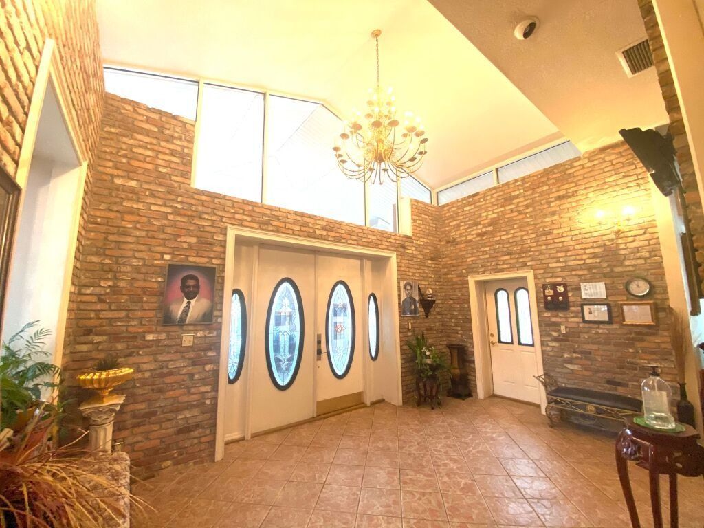 Entryway with brick walls, ornate doors, chandelier, and portraits.