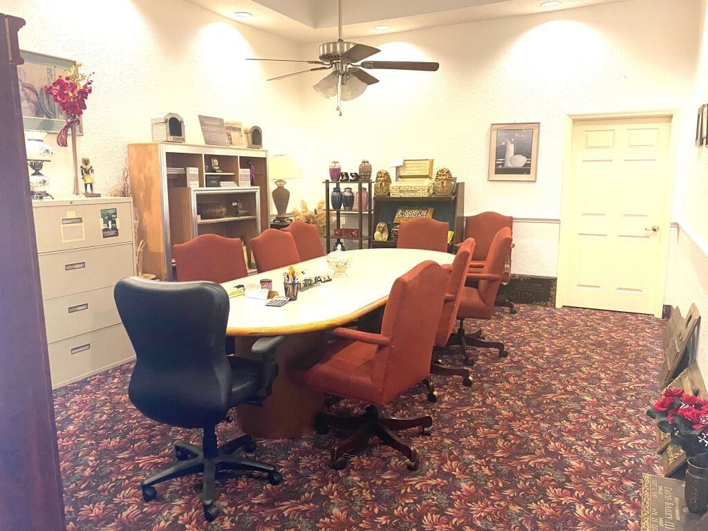 Conference room with oval table, red chairs, filing cabinet, and a closed door.