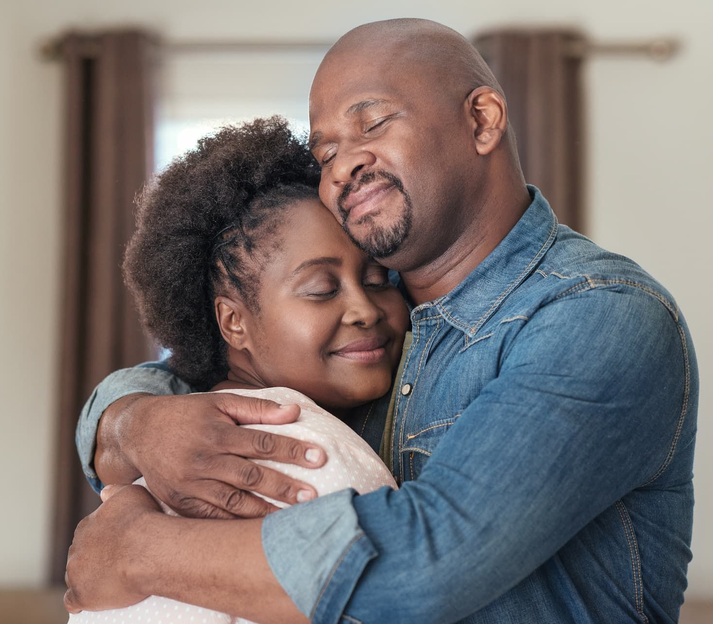 Couple embraces indoors, eyes closed, expressing affection.