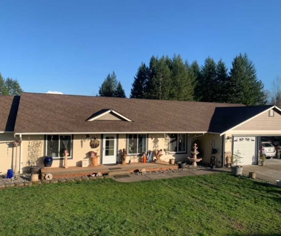 A house with a brown shingle roof is surrounded by trees