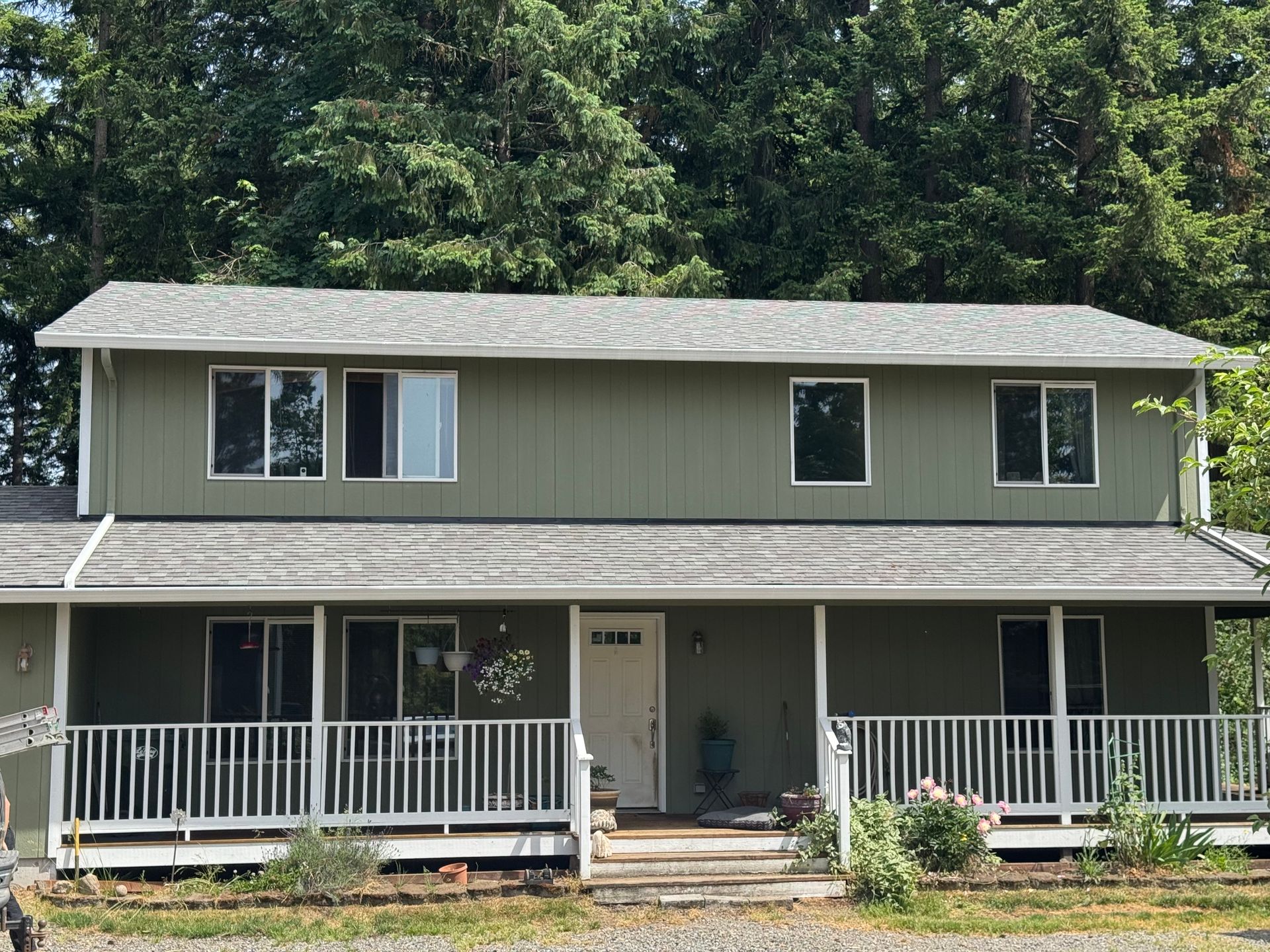A green house with a white porch and trees in the background
