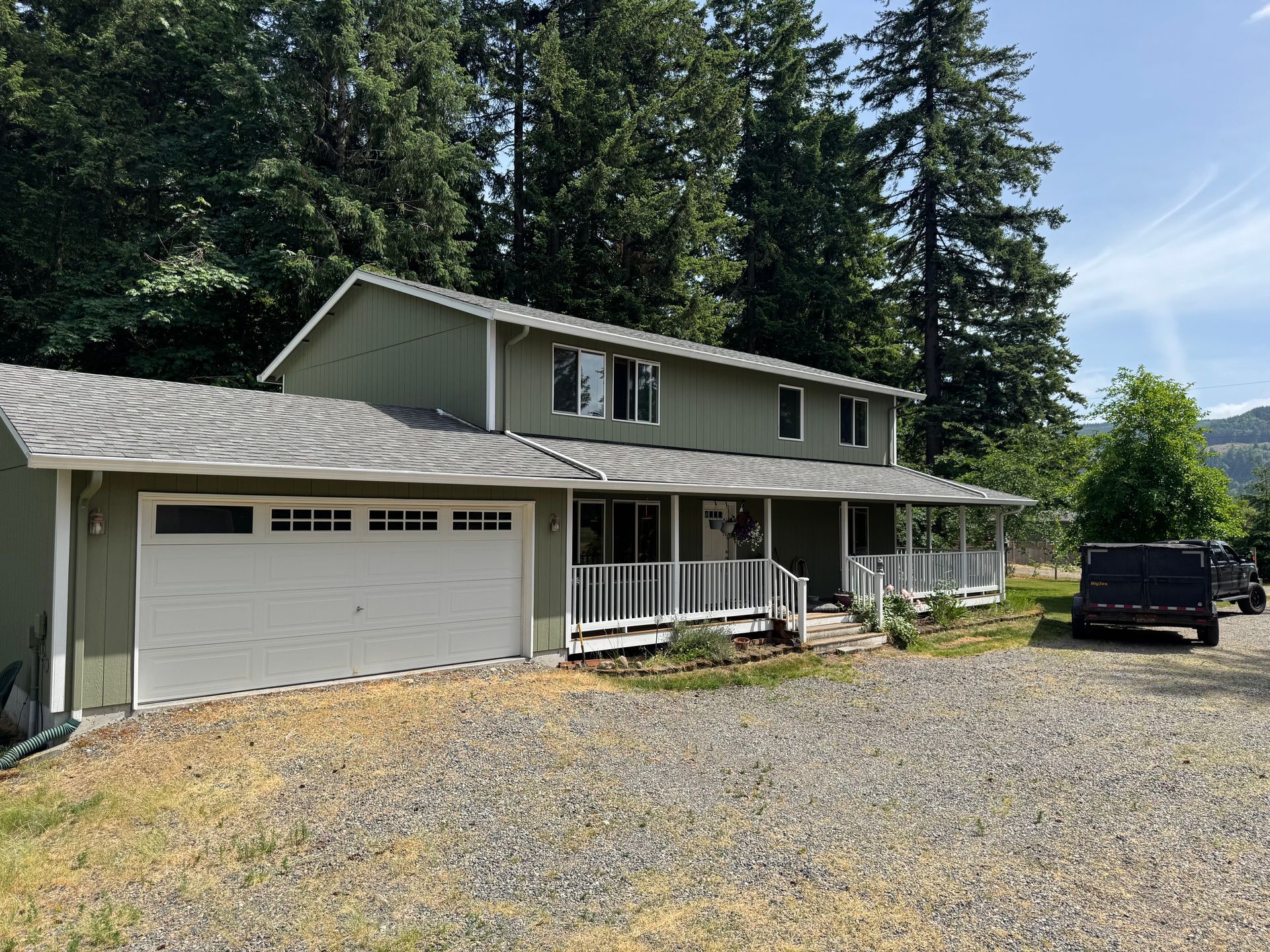 A house with a garage and a porch is surrounded by trees.