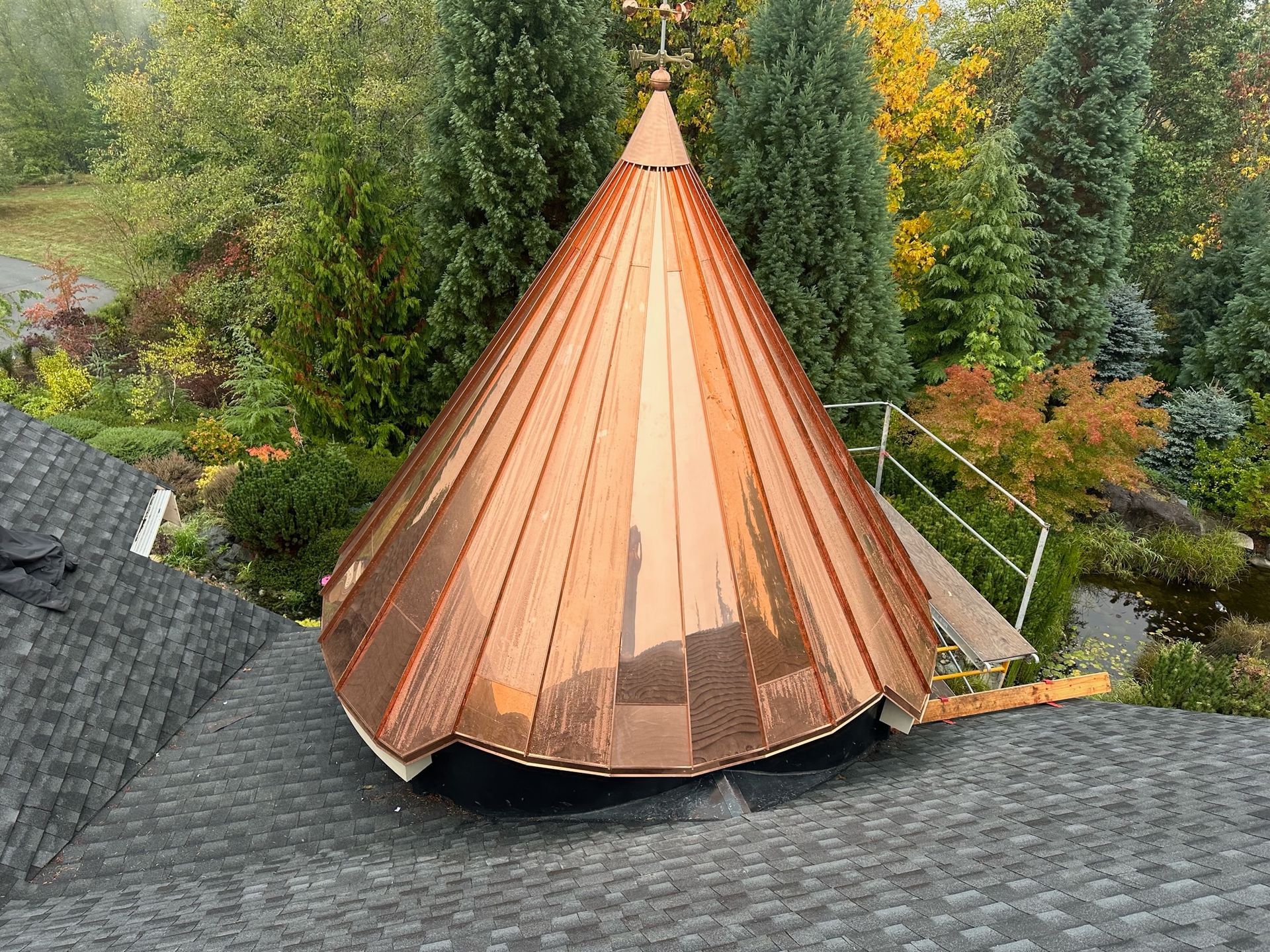 A copper dome is sitting on top of a roof surrounded by trees.