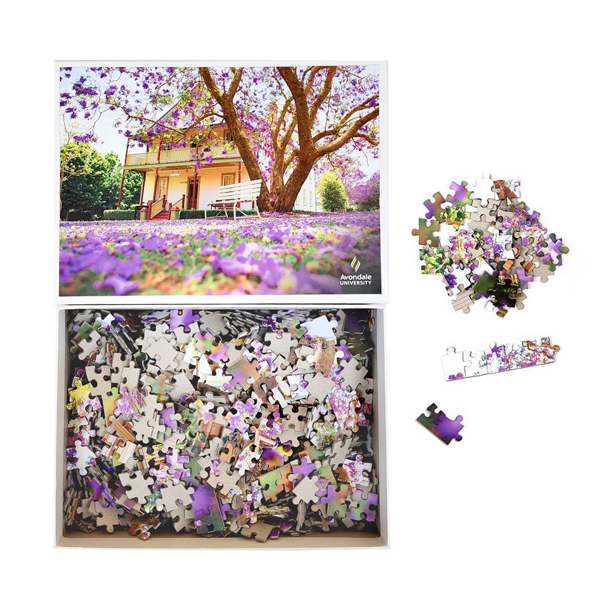 Puzzle box with a picture of a house under a purple flowering tree and a partially assembled puzzle.
