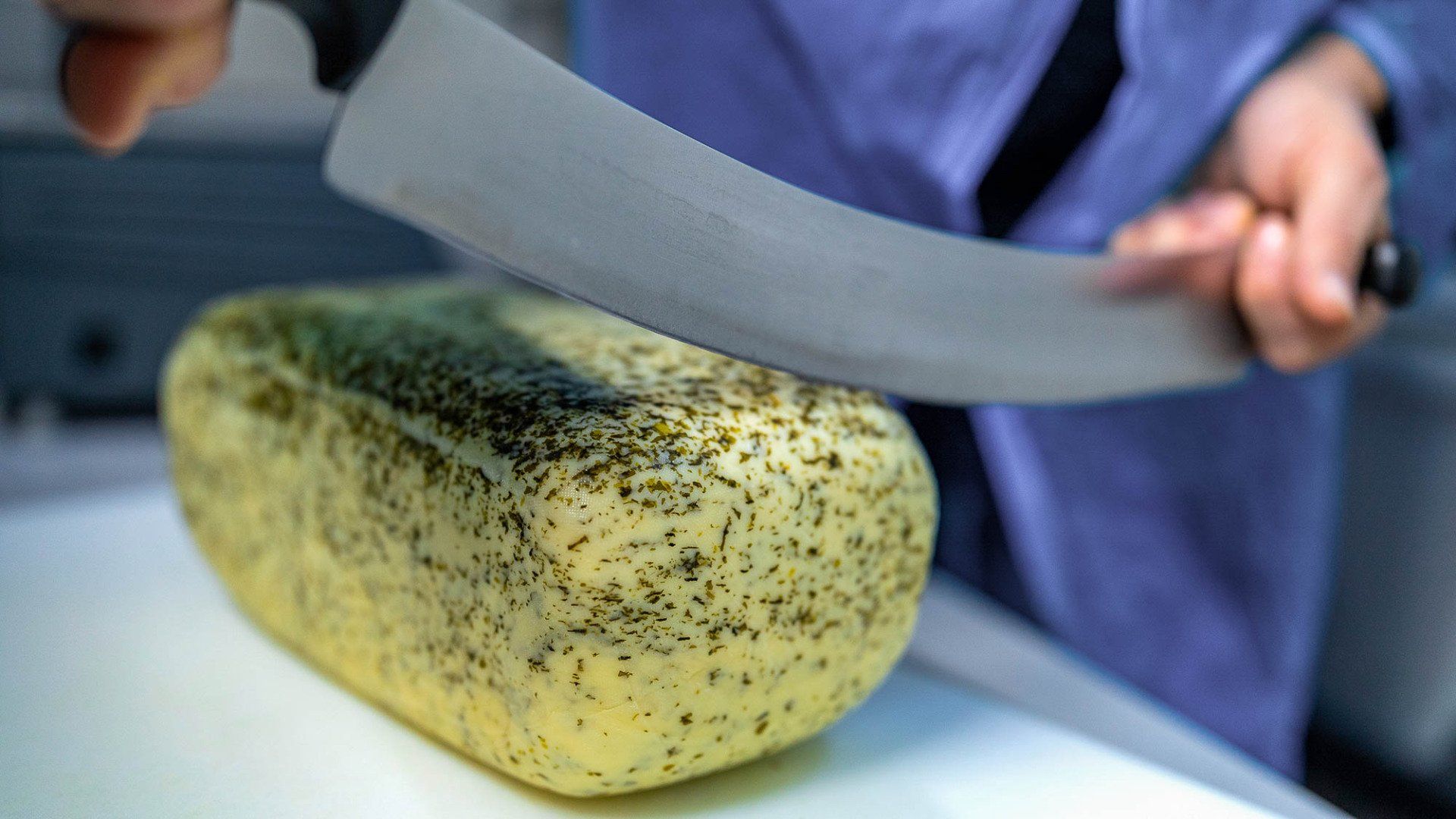Eine Person schneidet einen Laib Käse auf einem Schneidebrett