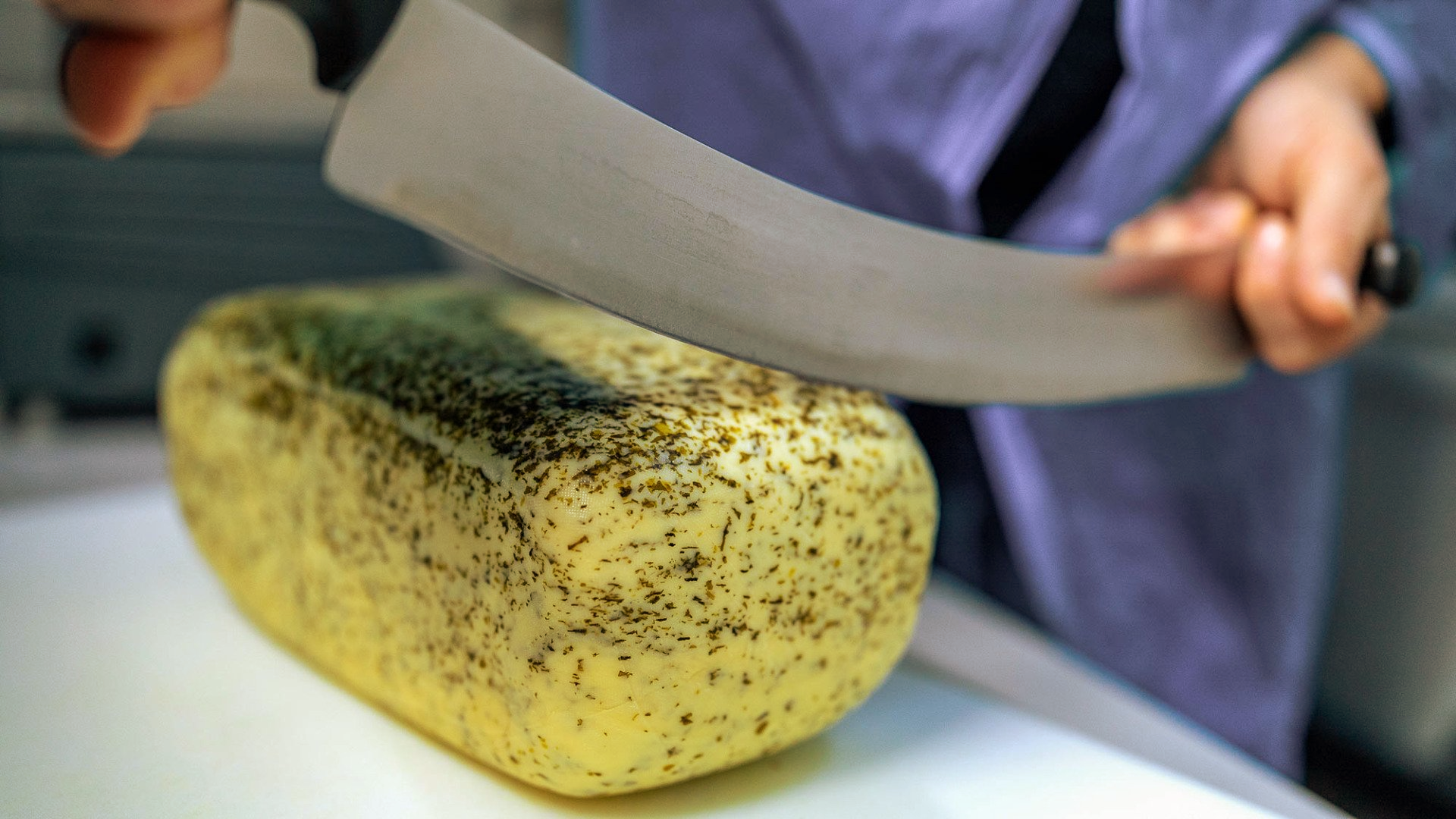 Eine Person schneidet einen Laib Käse auf einem Schneidebrett.