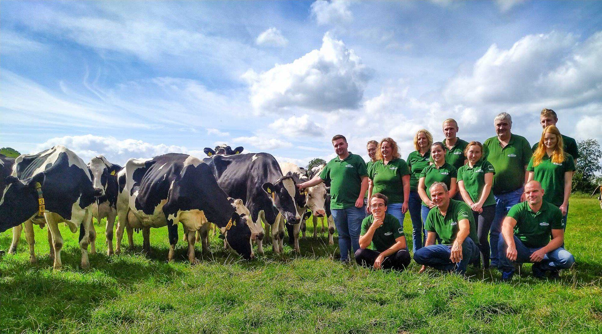Ein Teil des Engelnhof Teams steht in grünen T-Shirts neben einigen Kühen bei blauem Himmel auf der grünen Weide
