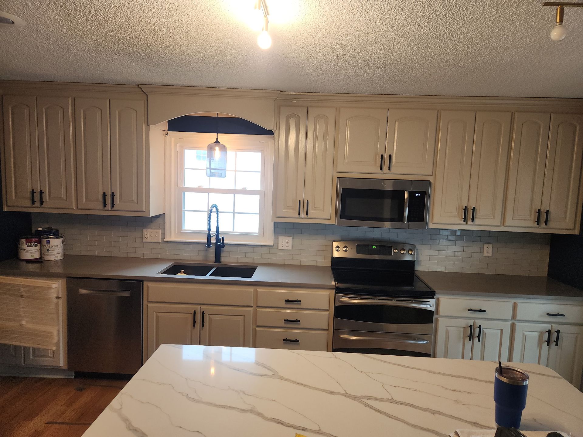 A kitchen featuring off-white cabinets, stainless steel appliances, a grey countertop, and a white marble-topped island.