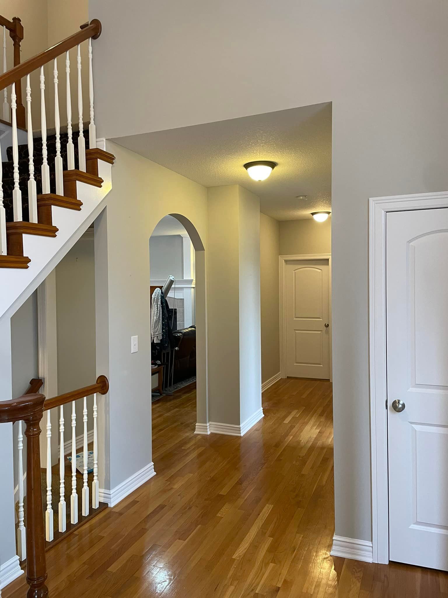 Hallway with hardwood floor, staircase, and arched doorway, leading to a door and living area.