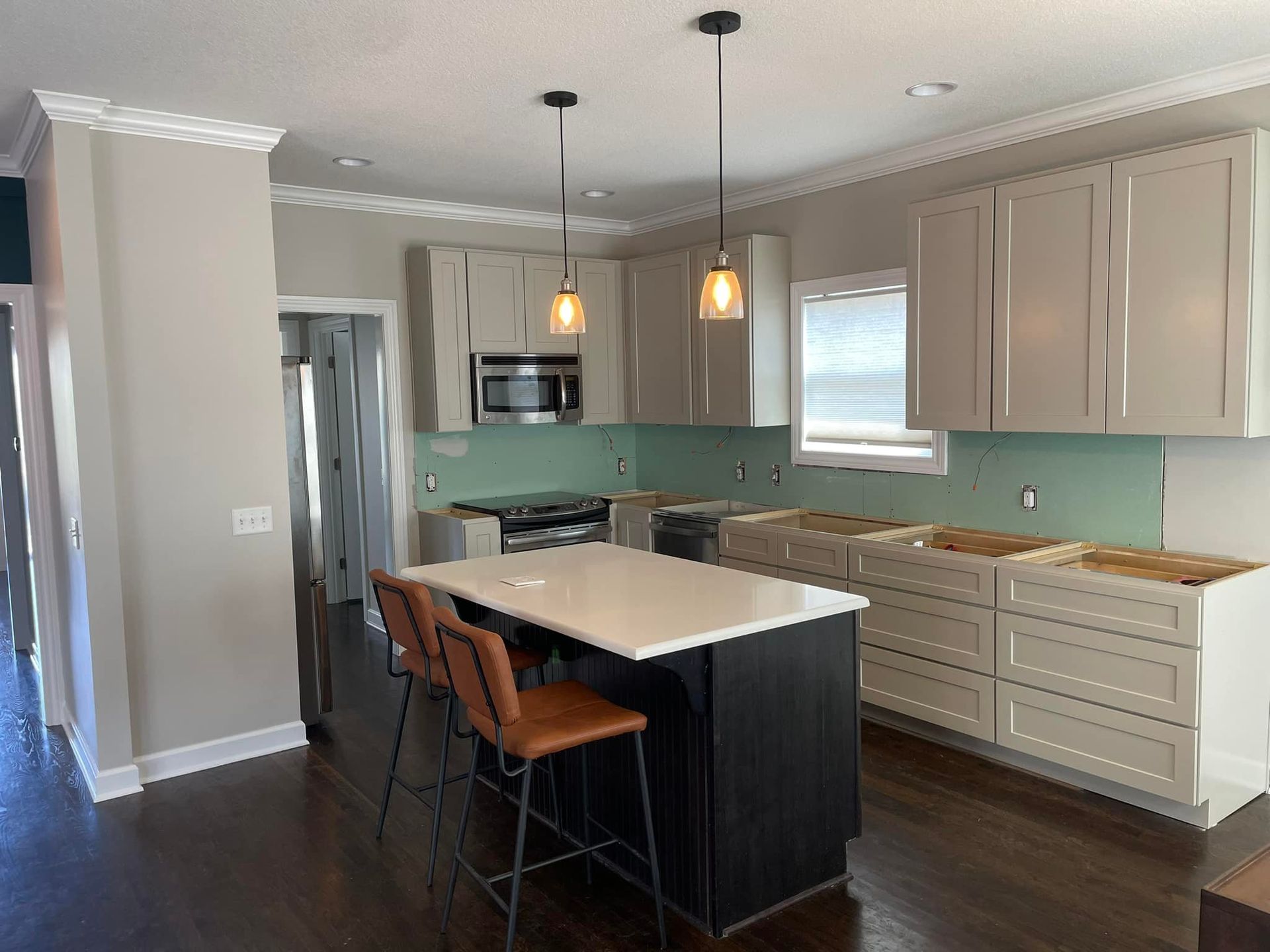 Kitchen undergoing renovation: light cabinets, turquoise backsplash, island with white countertop, brown bar stools.