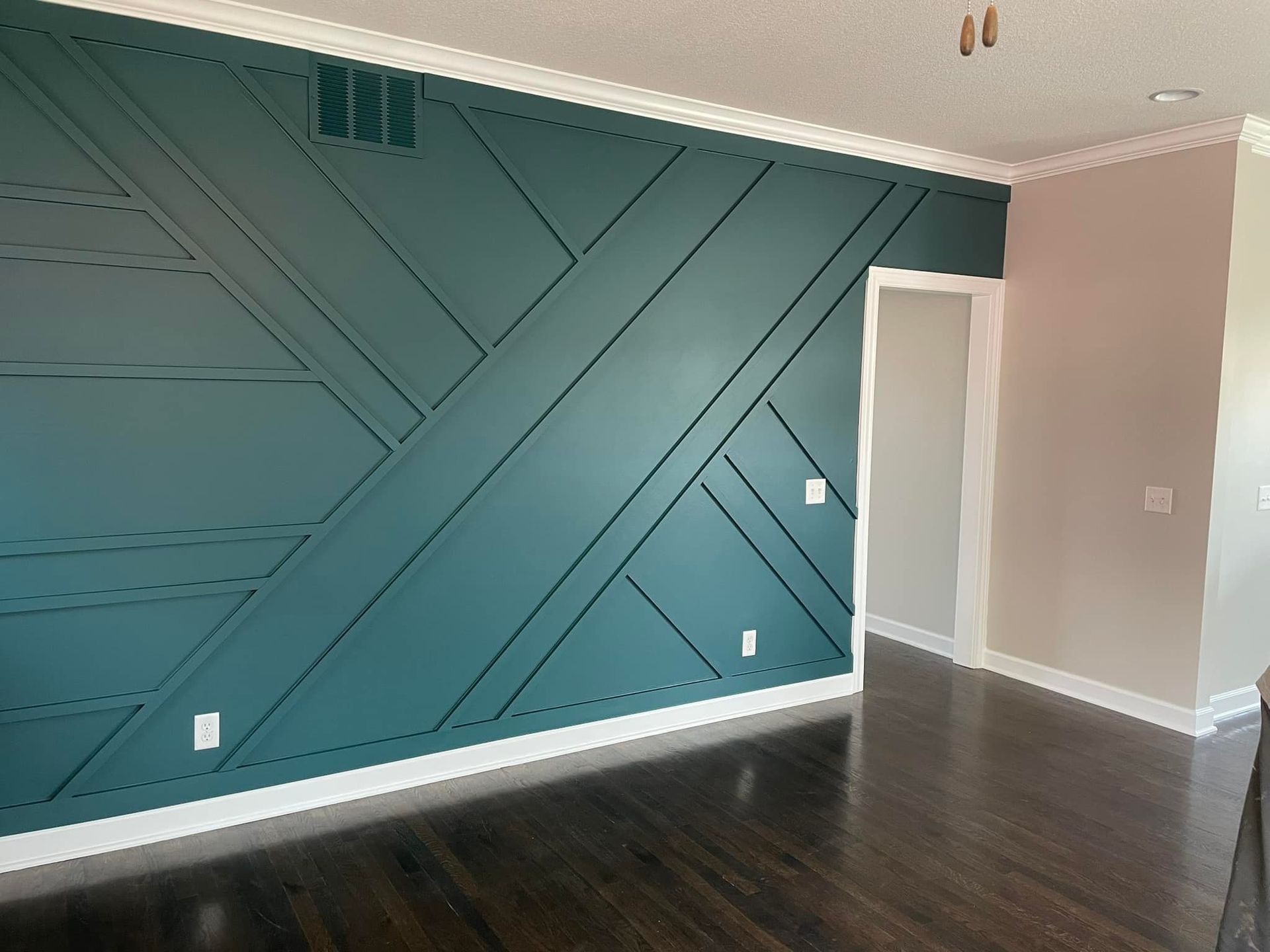 Teal accent wall with white trim and dark hardwood floors in a room.