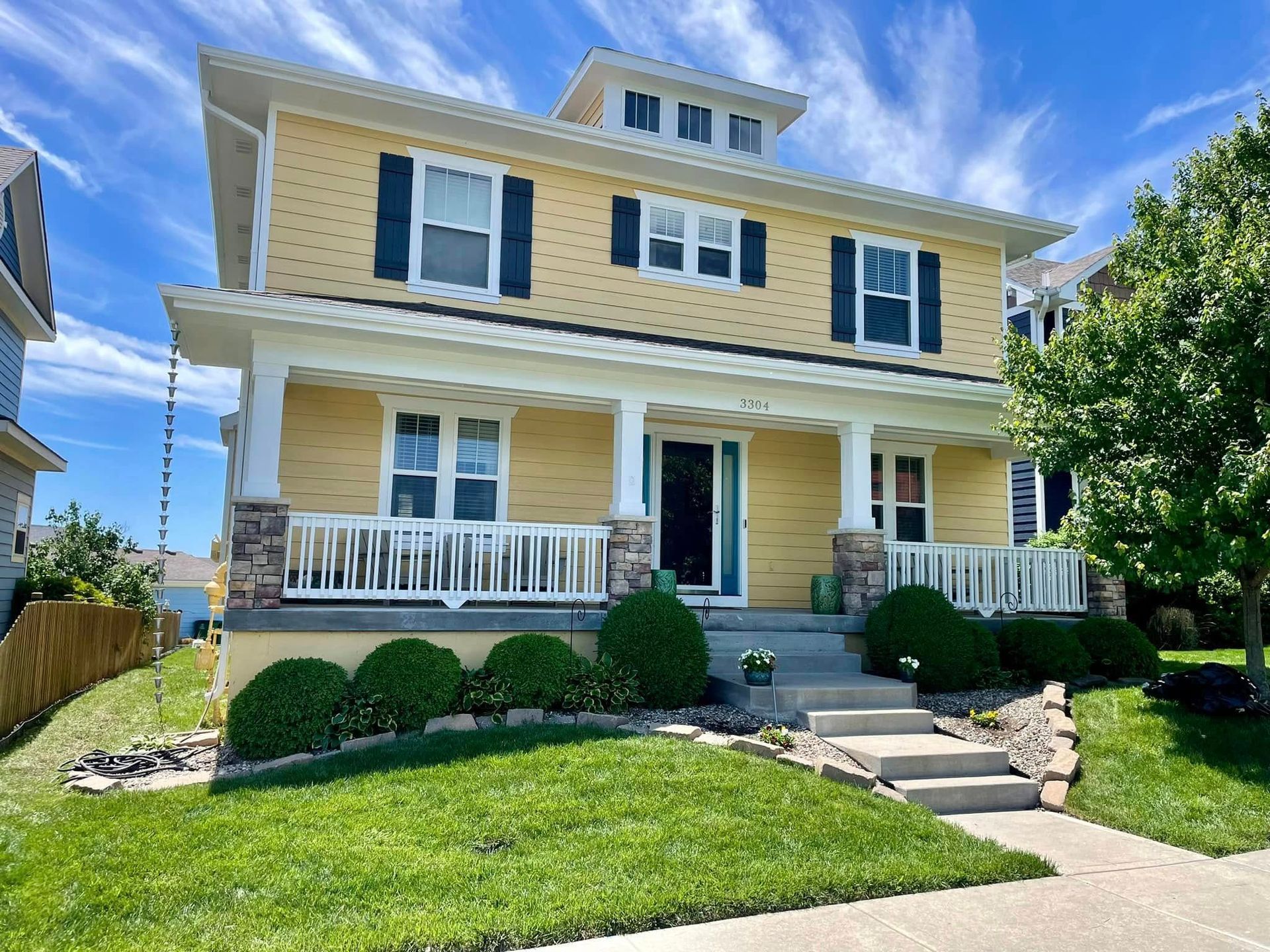 Yellow two-story house with white trim, porch, and blue shutters, under a bright blue sky.
