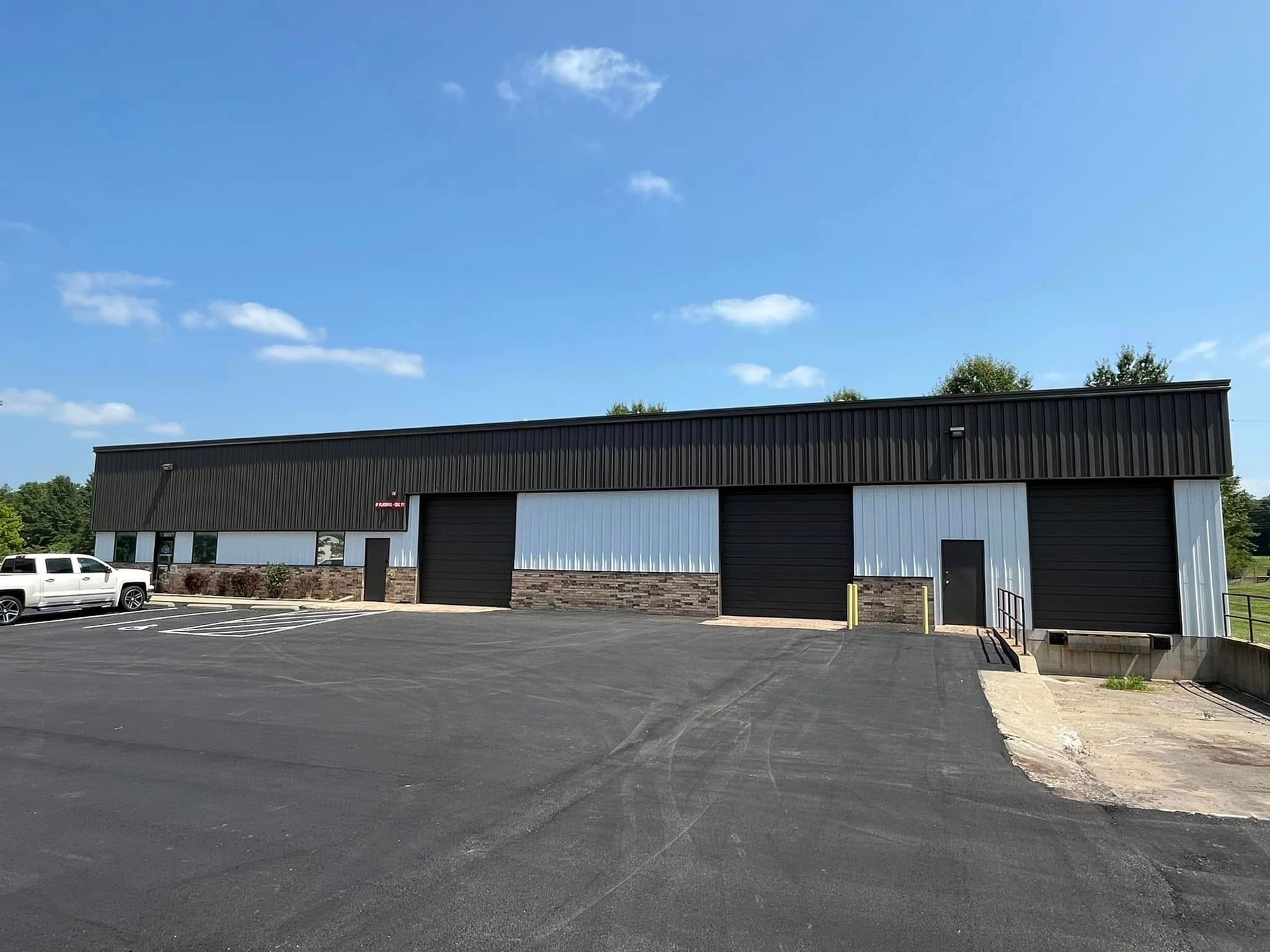 Commercial building with black doors, light siding, and a black roof against a blue sky.