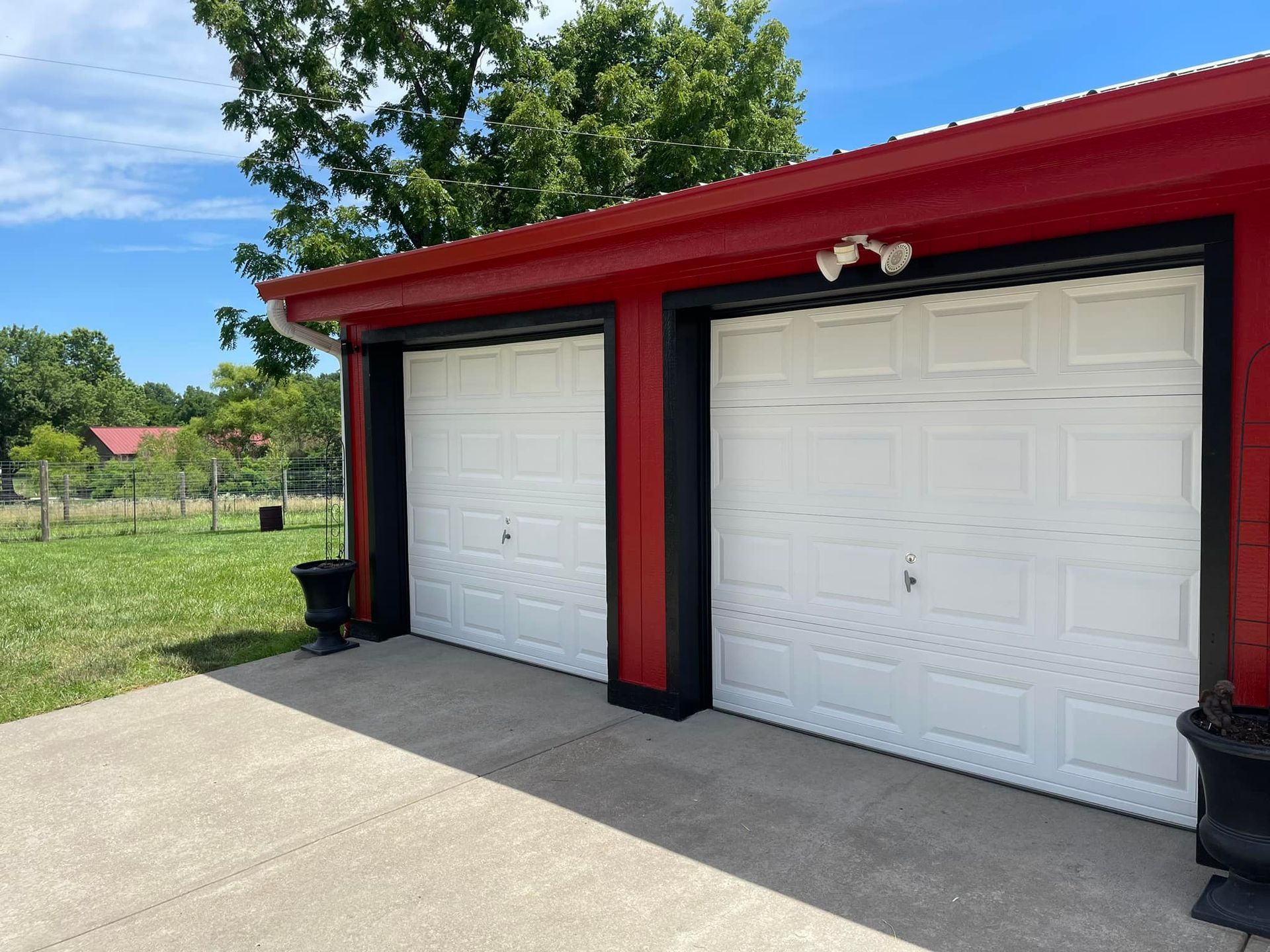 Two-car garage with white doors, red trim, and black outlining on a concrete driveway. Trees in background.
