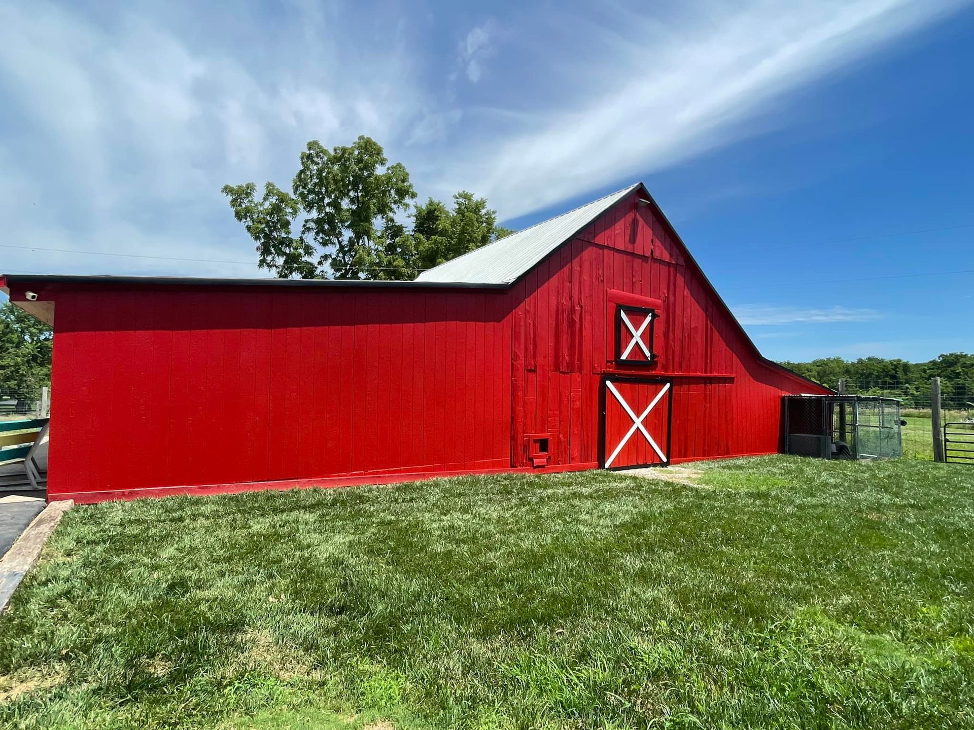 Red barn with white doors and roof, set against a blue sky with green grass.
