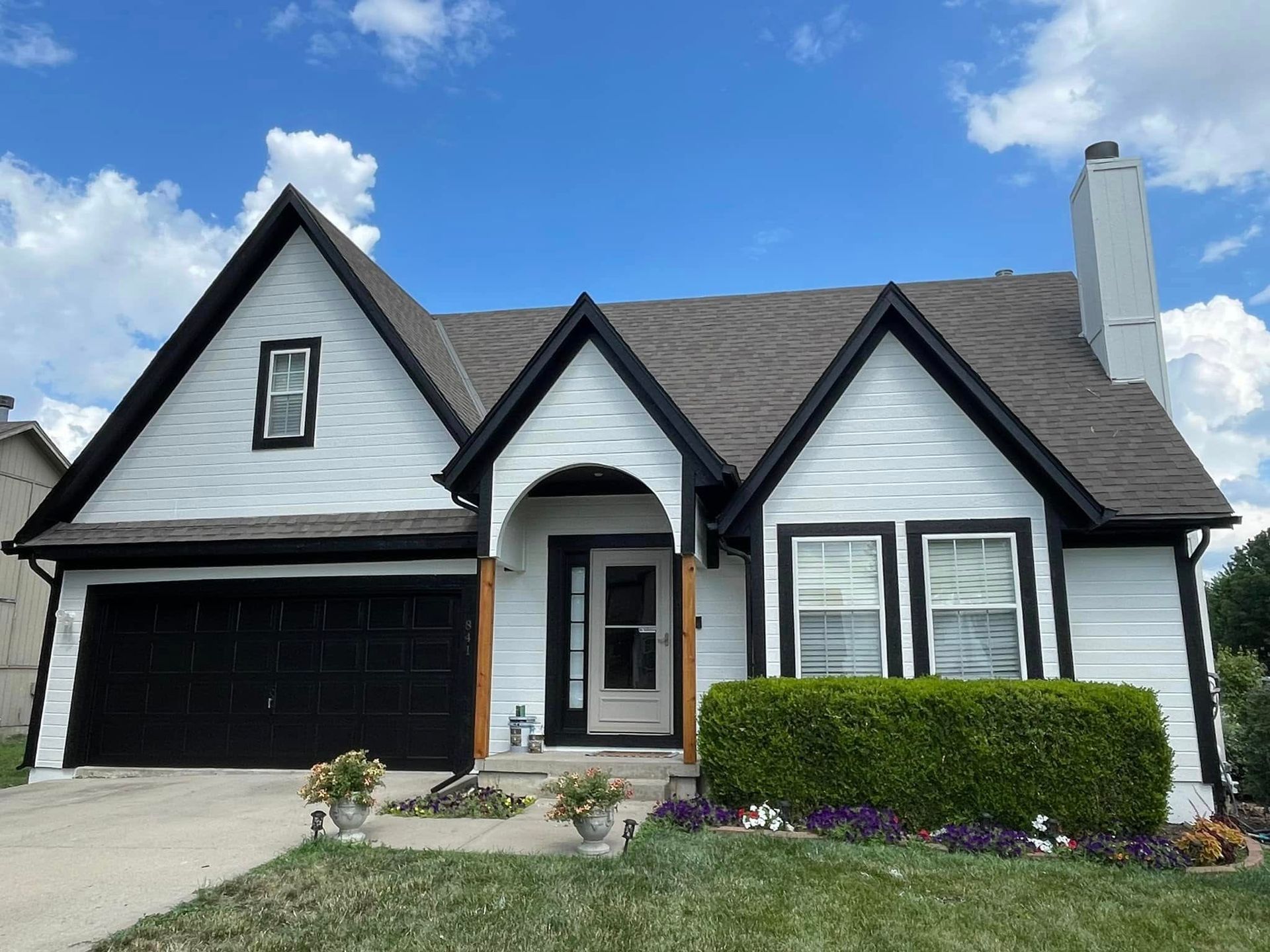 White house with black trim, garage, and roof against a blue sky with some clouds.