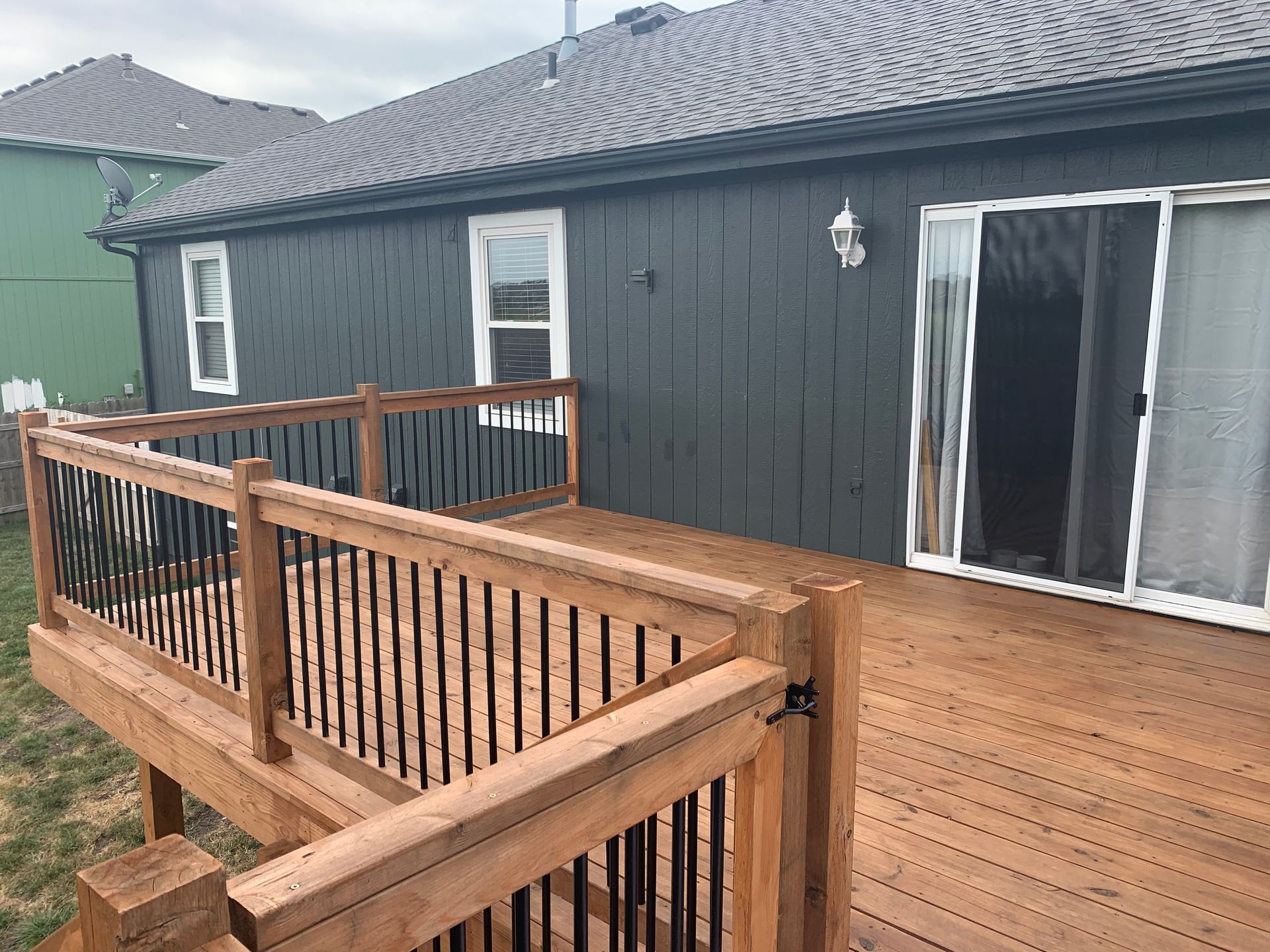A wooden deck with black metal railings extending from the back of a house with dark gray vertical siding.
