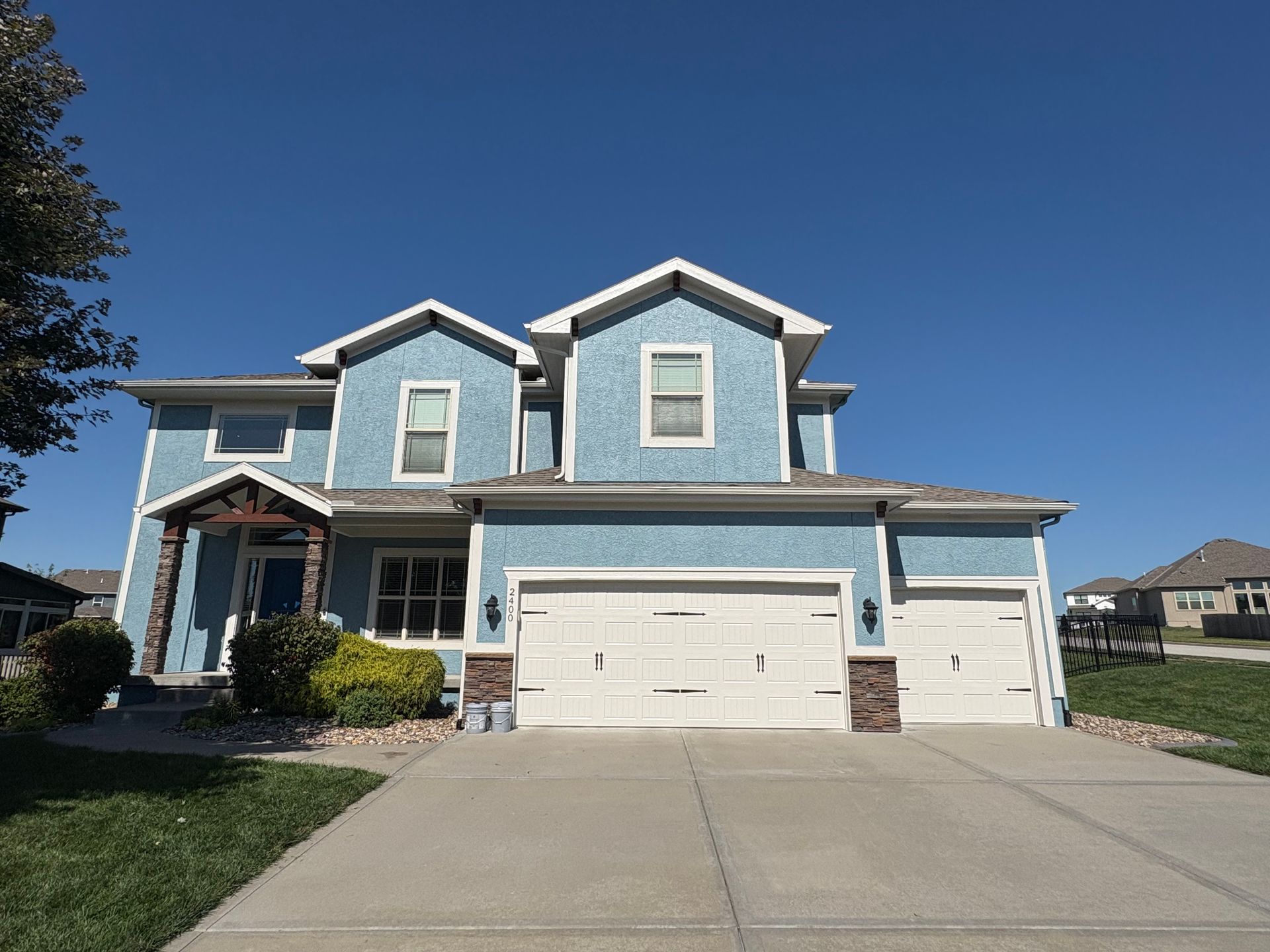 A blue two-story suburban house with a three-car garage and a concrete driveway under a clear blue sky.