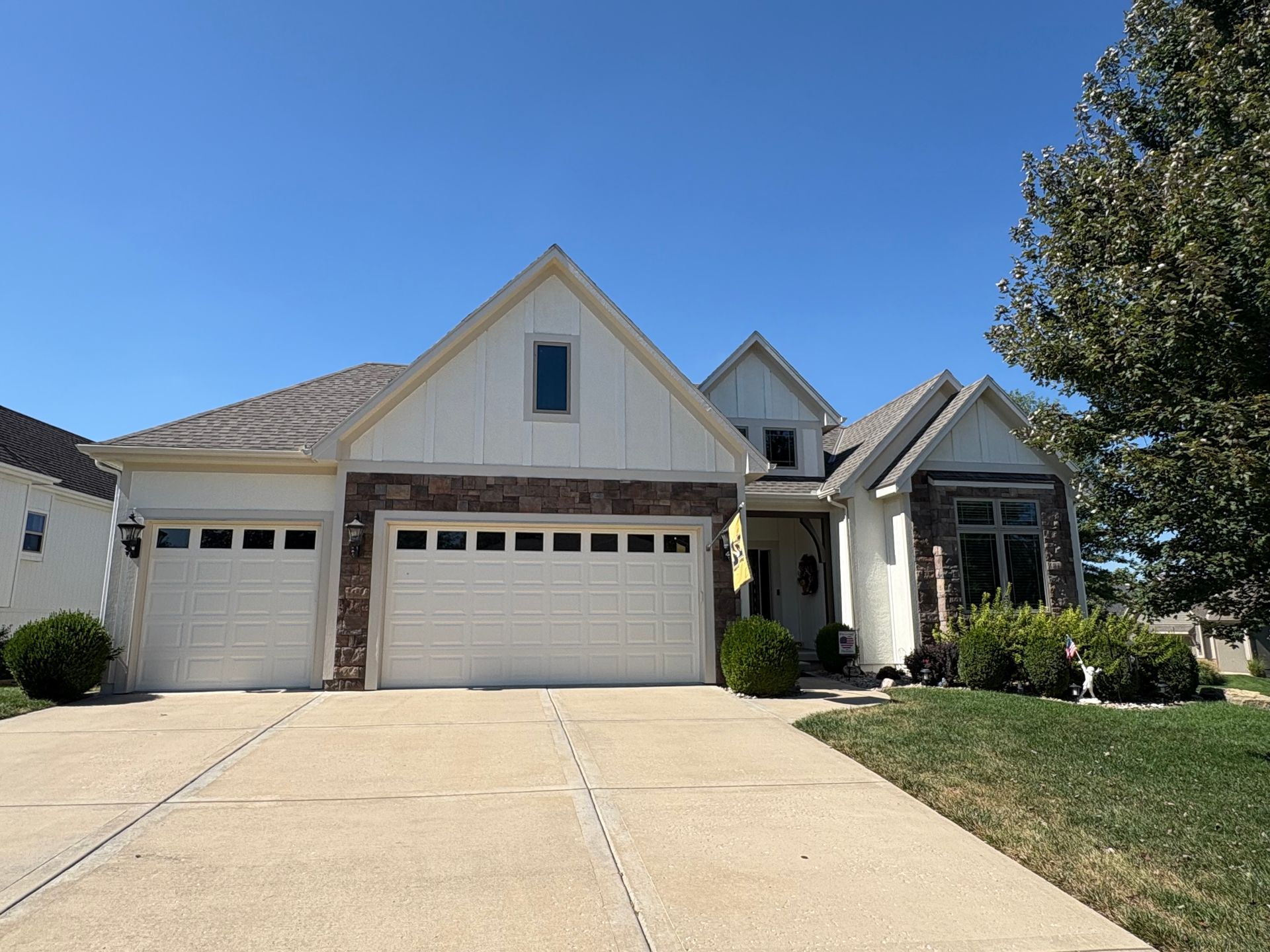 A modern suburban home with white vertical siding, stone accents, a three-car garage, and a concrete driveway.