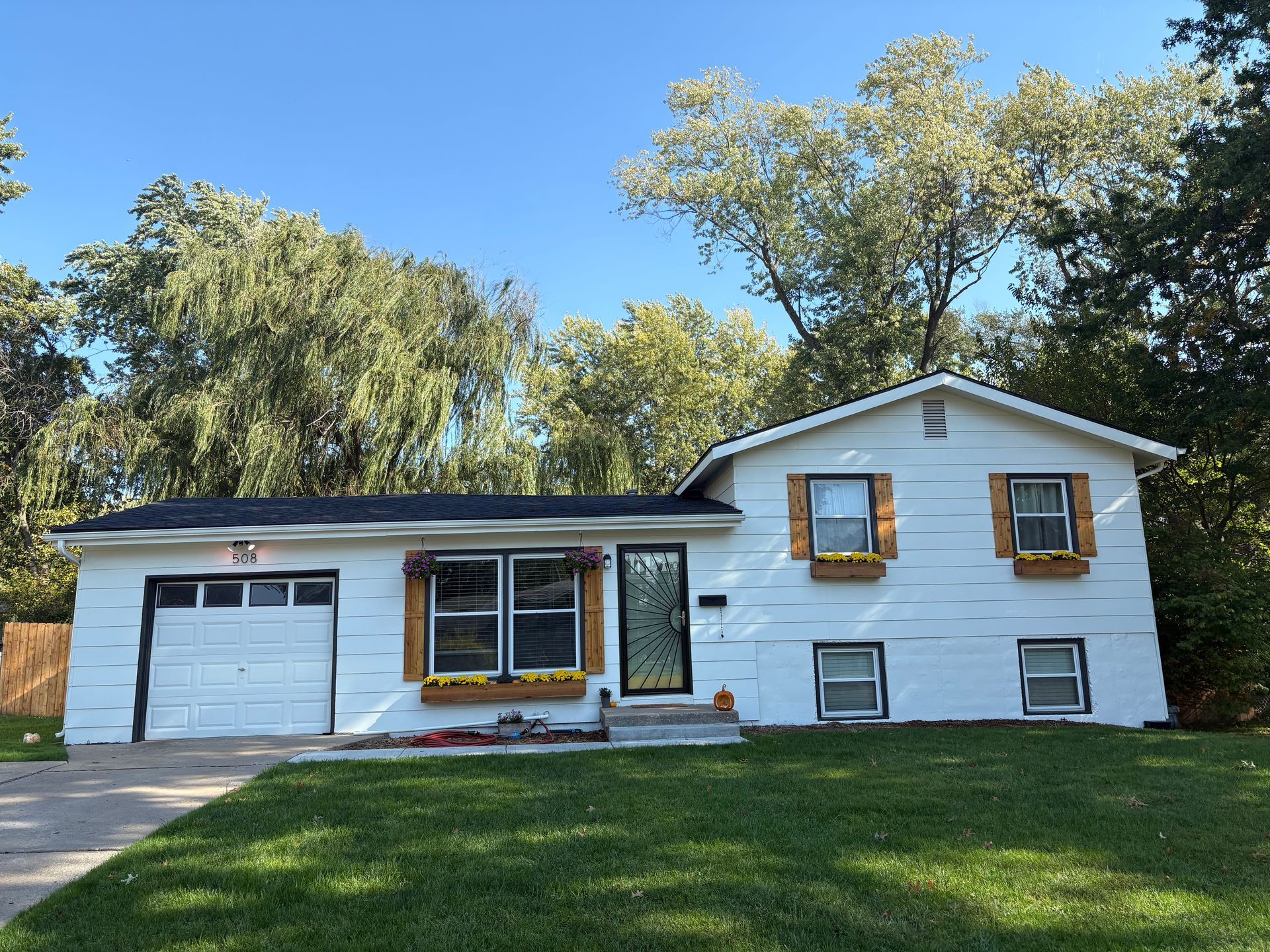 A one-story, white house with a garage, brown shutters, and window boxes, set against a green lawn and trees.