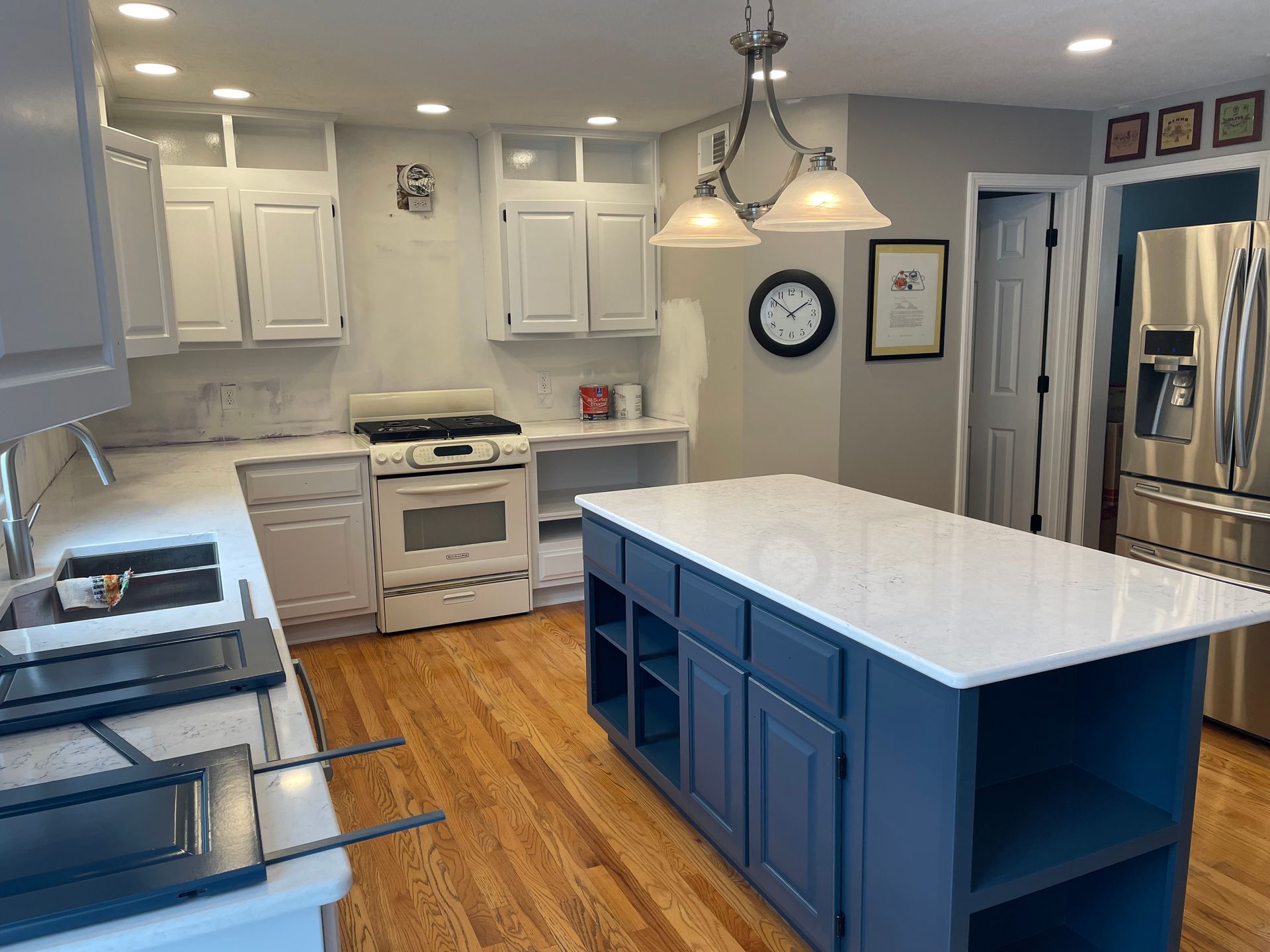 A modern kitchen with white cabinets, a navy blue island, white countertops, and hardwood floors.