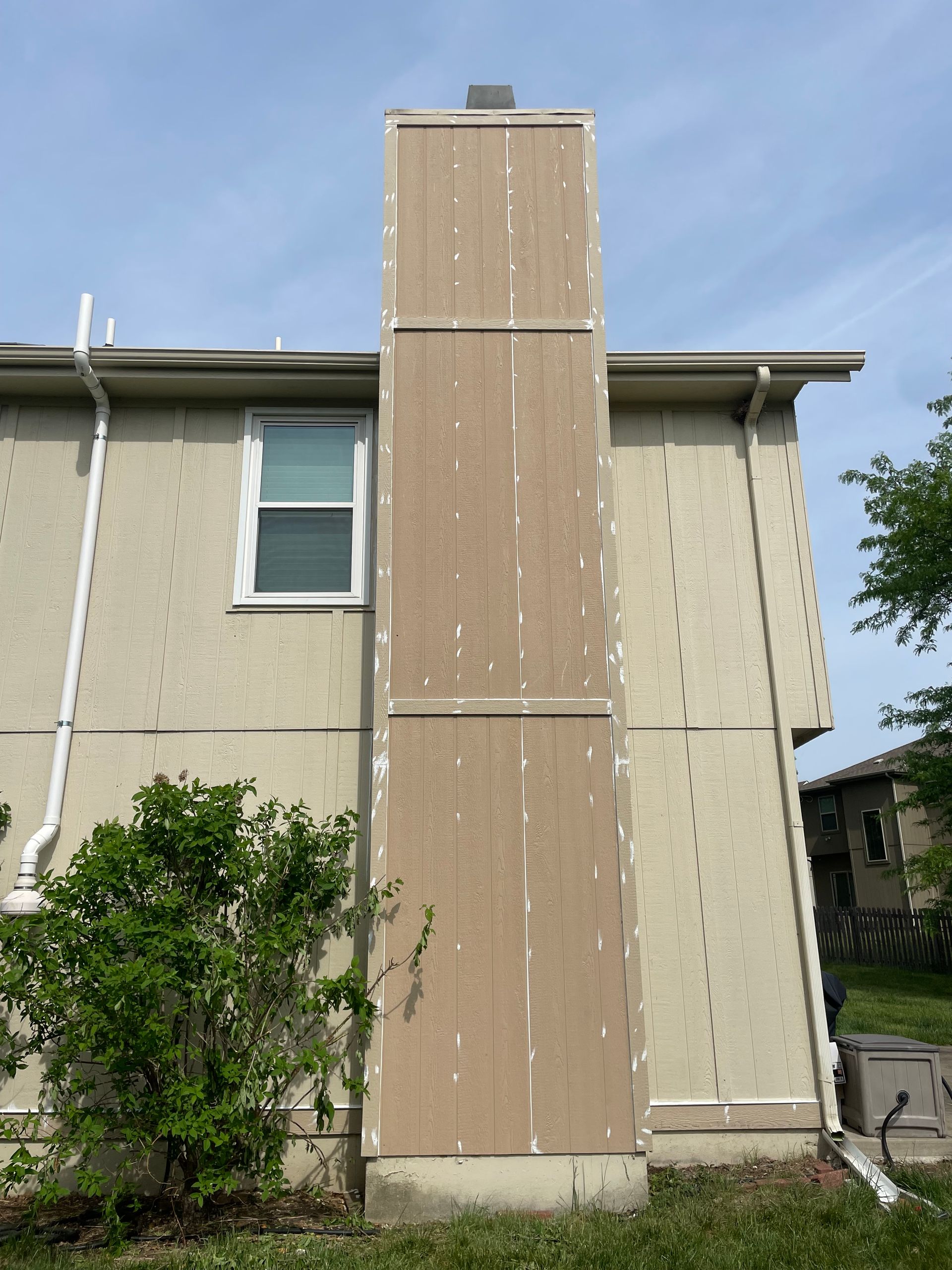A tan exterior wall of a building with a chimney and downspout under a blue sky.