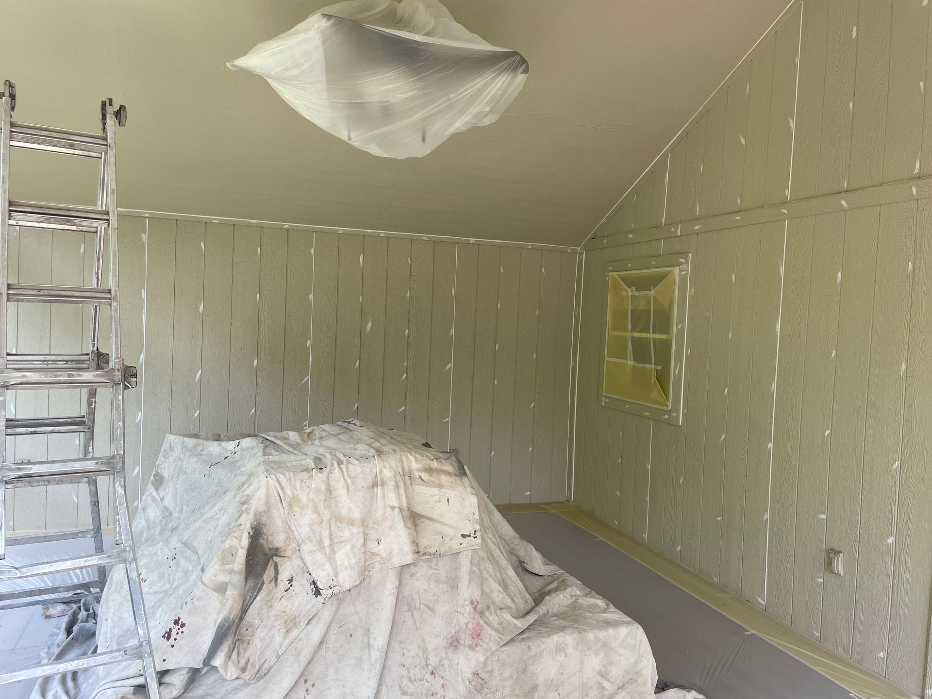 An interior room under renovation with walls masked in painter's tape, a ladder to the left, and a drop cloth on the floor.