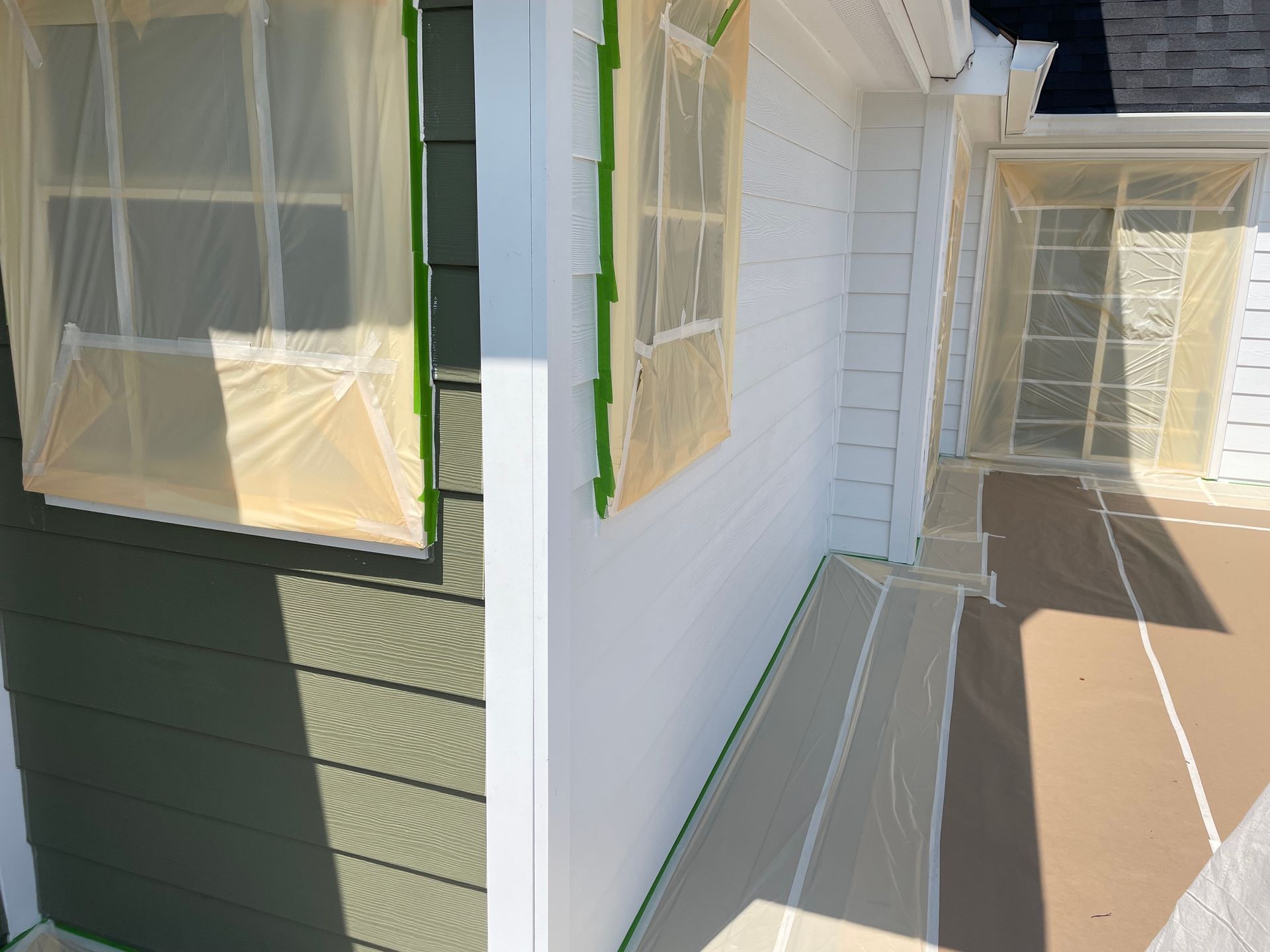 Exterior walls and windows prepared for painting, with protective plastic covering windows and surfaces on a patio.