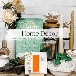 Home decor arrangement with flowers, books, candles, and a small orange door against a white wood backdrop.