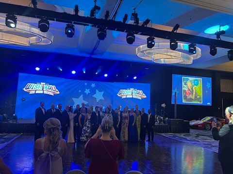 A group of people are standing on a dance floor in front of a large screen.