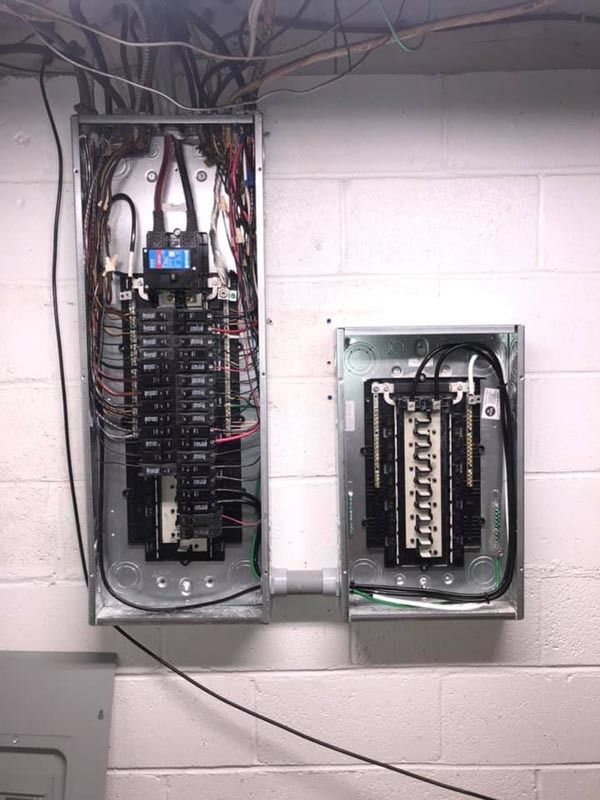 Two metal electrical panels mounted on a white wall, connected by a conduit.