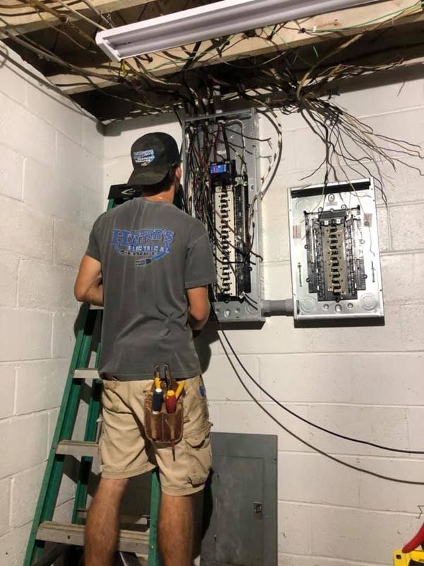 Electrician working on electrical panel in a basement. Wires, tools visible.