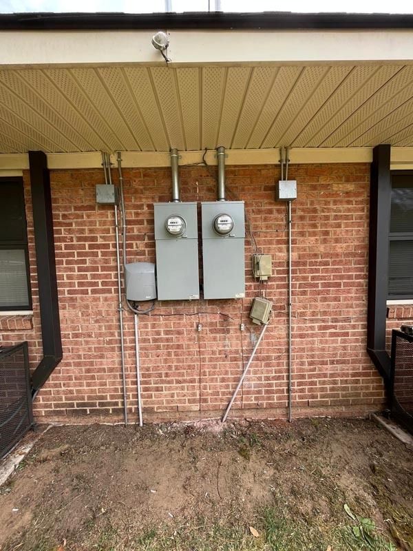 Electrical meters and boxes mounted on a red brick exterior wall beneath a beige overhang.