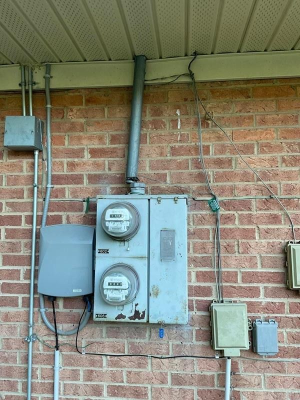 Electrical meters and boxes mounted on a brick wall beneath a light-colored overhang.