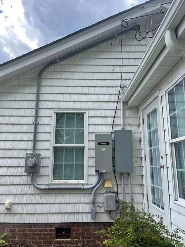 Exterior view of a house with electrical components: meter box, conduit, water heater, and service panel.