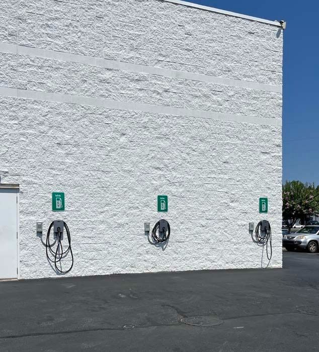 Three electric vehicle charging stations mounted on a white textured building. Dark cables hang down.