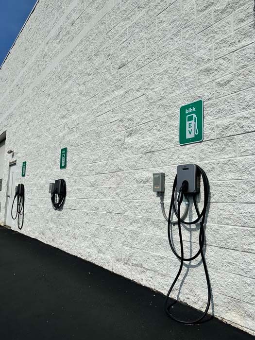 Electric vehicle chargers mounted on a white brick wall, with green signs indicating their use.