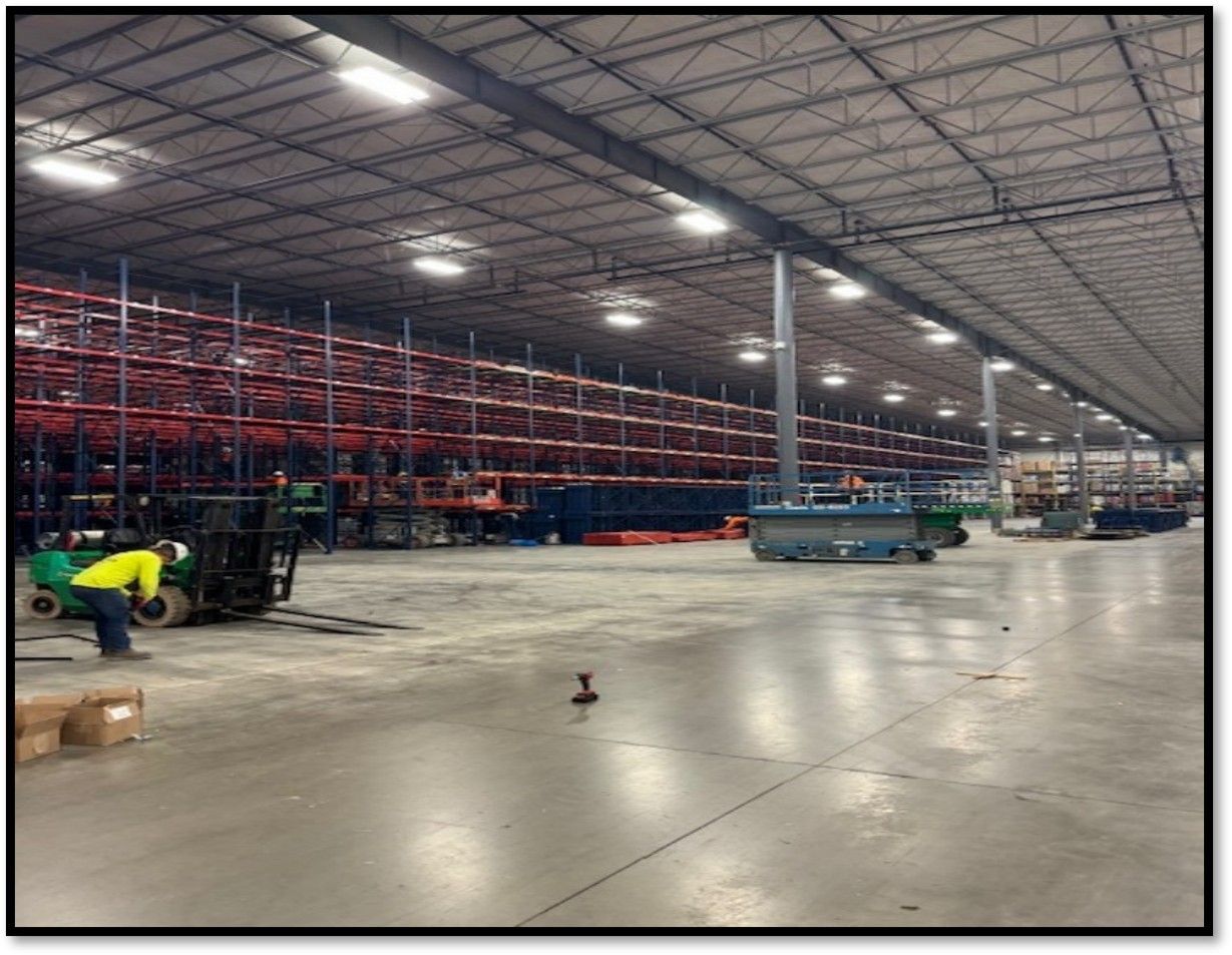 Warehouse interior with tall shelving. A person in a yellow vest operates a forklift.