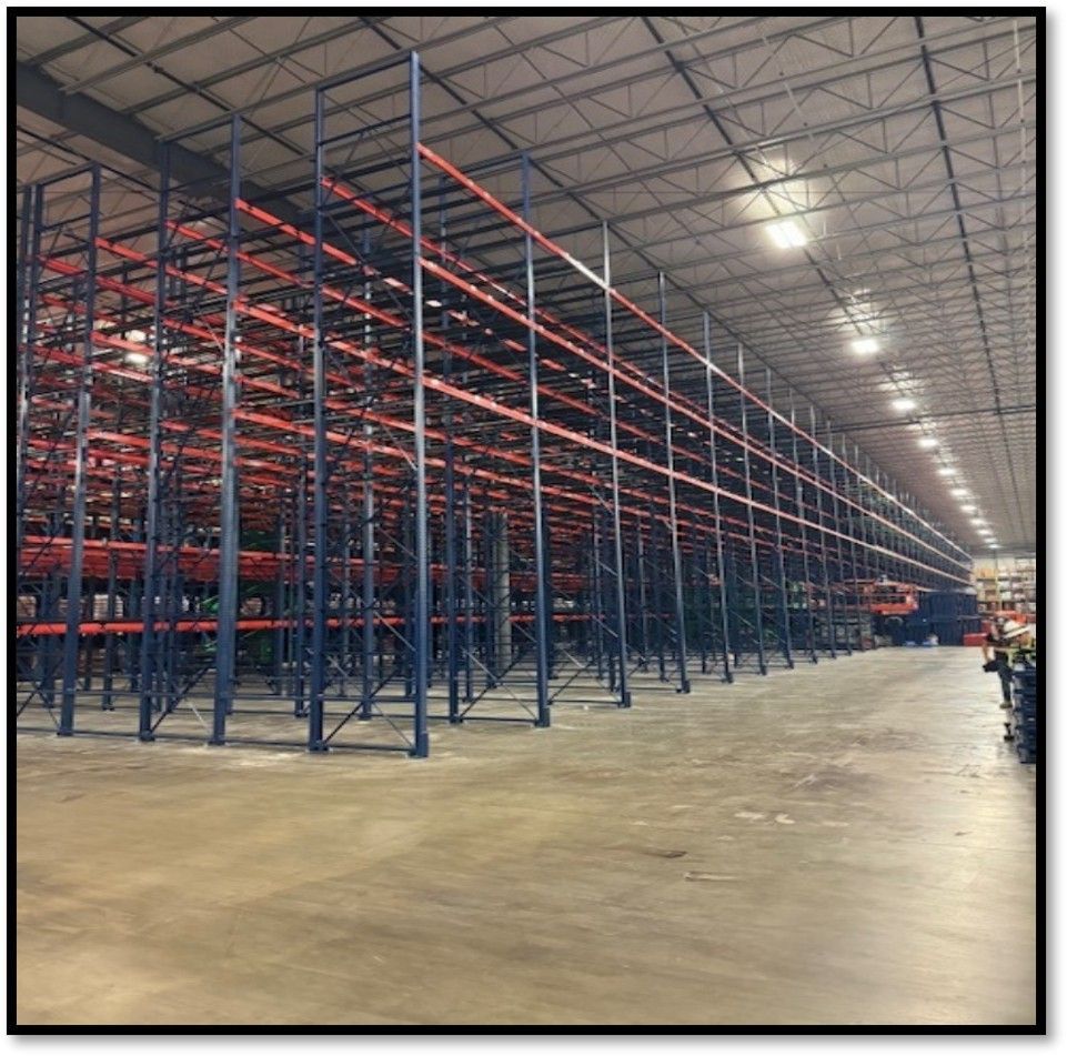 Empty warehouse with tall blue and red industrial shelving. Concrete floor.