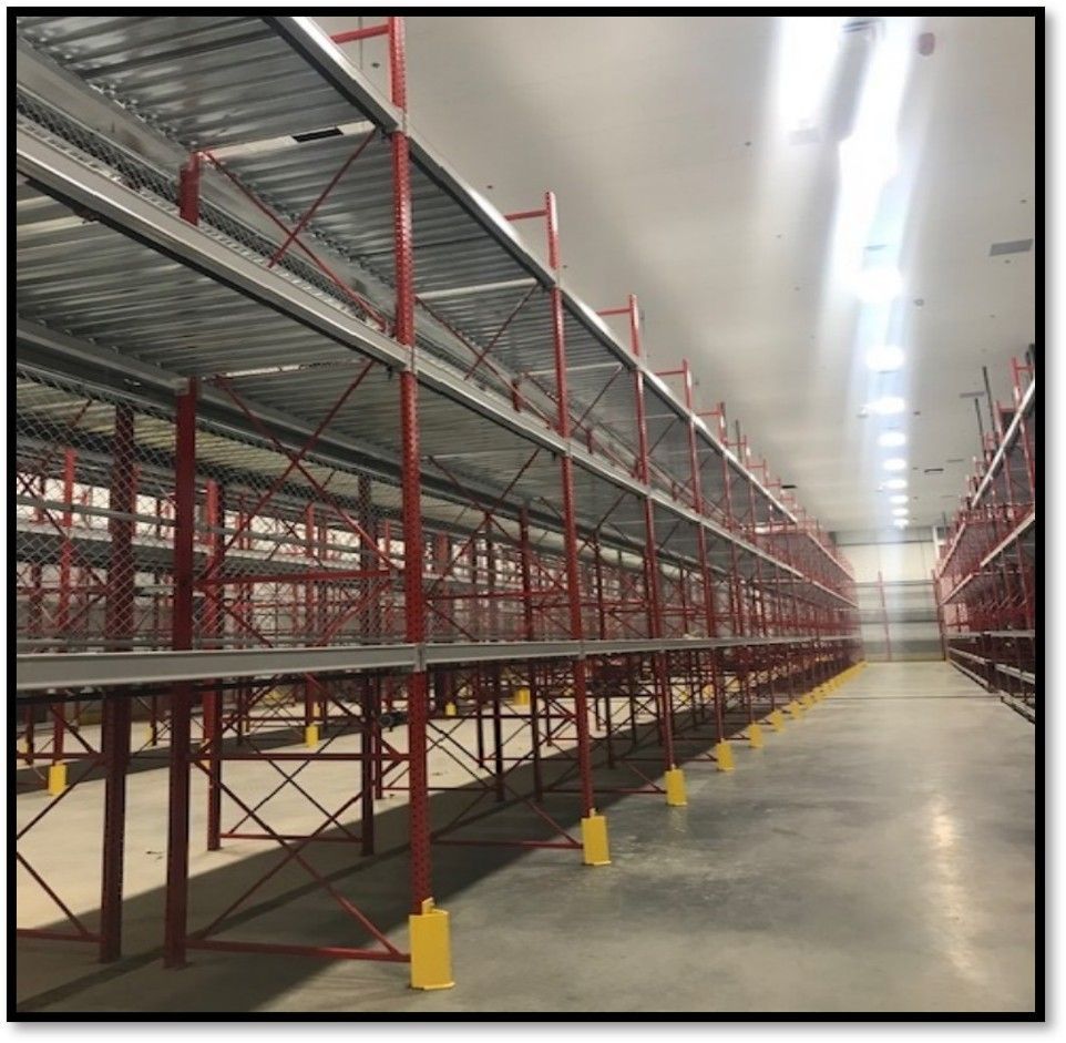 Warehouse interior with long metal shelving units; red frames, silver shelves, concrete floor.