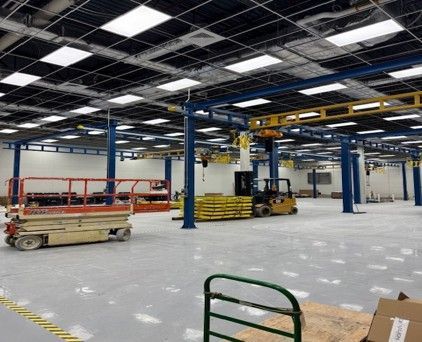 Large industrial interior with lifts, forklift, and overhead crane system. Blue support beams, yellow crane track.