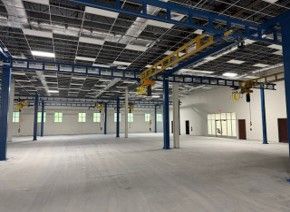 Empty industrial warehouse with blue support beams, yellow cranes, and white walls.