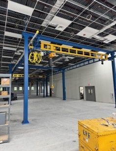 Blue and yellow overhead crane system in a large, empty industrial building.